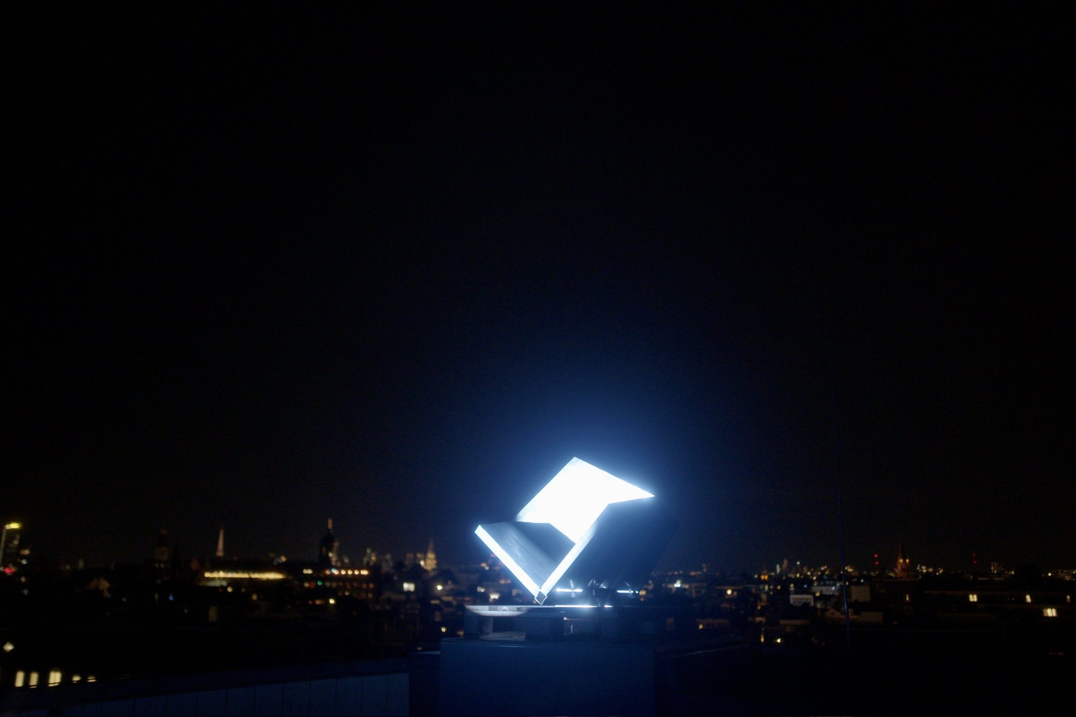 An illuminated radar reflector on an Amsterdam rooftop at night, the city skyline behind it